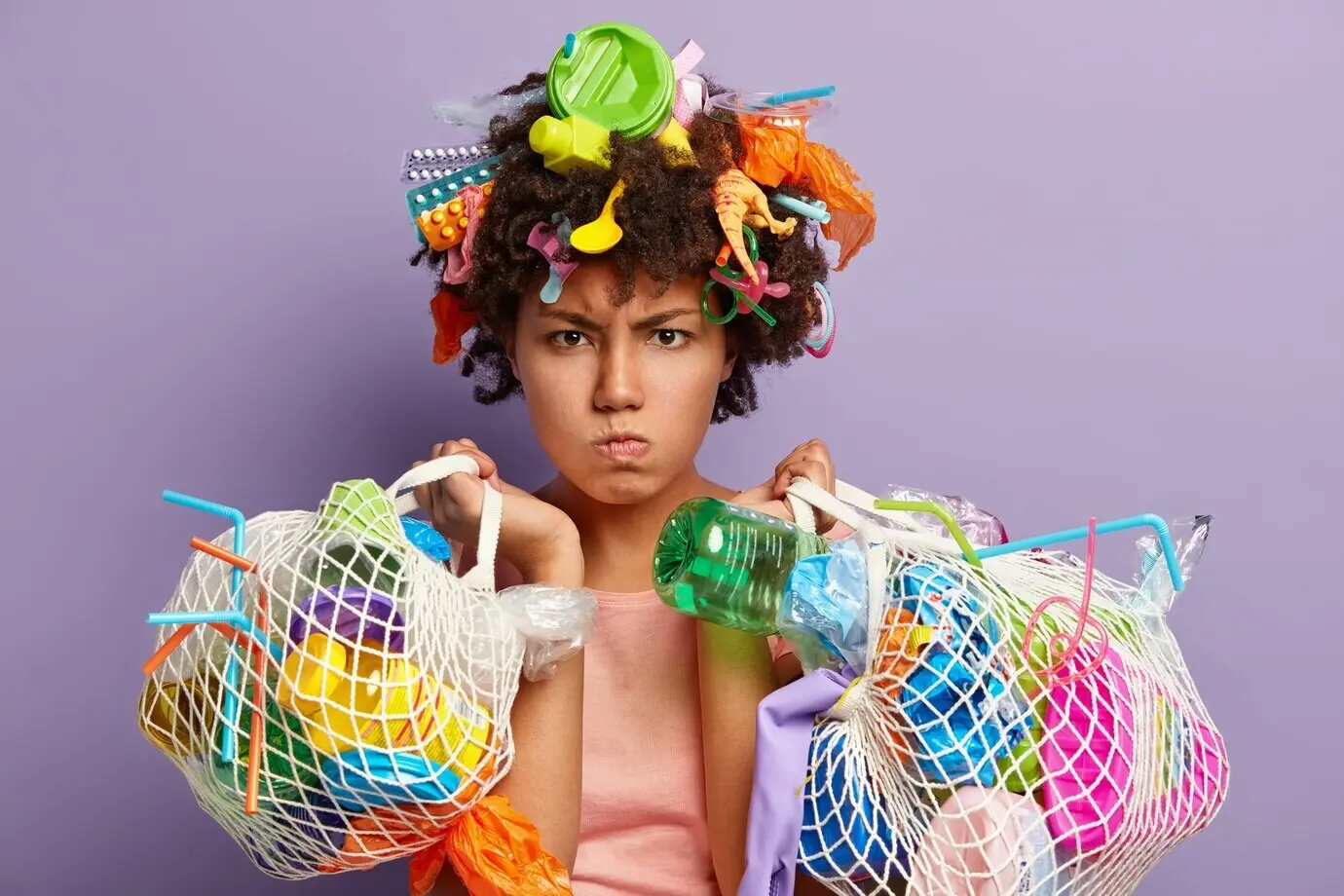 Foto eines gereizten weiblichen Models mit wütendem Gesichtsausdruck, dem die Sauberkeit unseres Planeten am Herzen liegt; sie trägt Plastikmüll, sammelt während des Earth Day Müll auf und kämpft gegen Kontamination oder Verschmutzung.