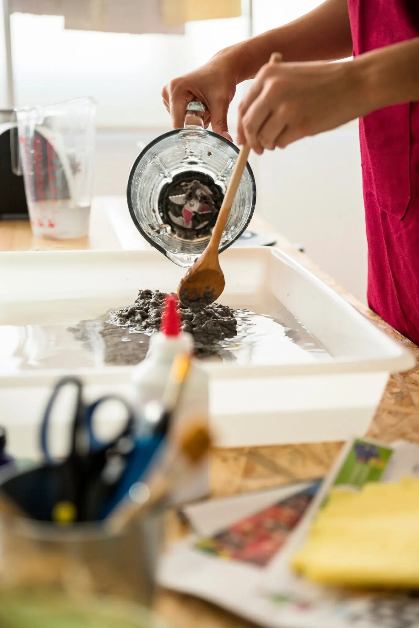 Eine Frauenhand rührt Papiermasse im Wasser um.